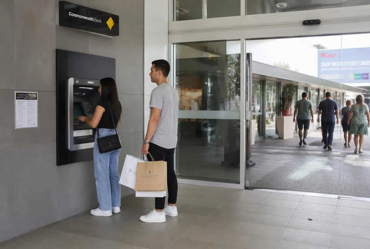 Wall-mounted ATM built into the wall beside the entrance of an Australian shopping centre with shoppers using it